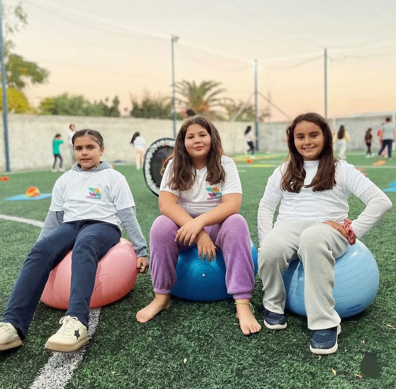 Tres niños sonrientes sentados en pelotas de gimnasia al atardecer en una actividad de EduKinesis en Paso de los Toros